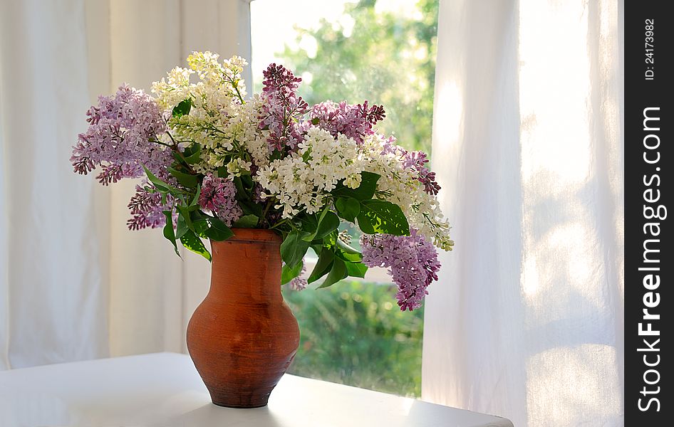 Bunch of lilac in ceramic jug against summer window. Bunch of lilac in ceramic jug against summer window