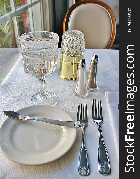 Silverwear, a folded napkin and a crystal glass filled with water on a restaurant table. Silverwear, a folded napkin and a crystal glass filled with water on a restaurant table