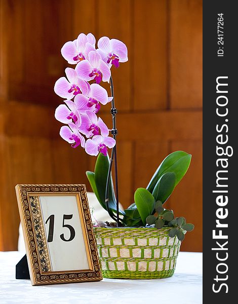 A purple orchid flower centerpiece with a framed table number. A purple orchid flower centerpiece with a framed table number