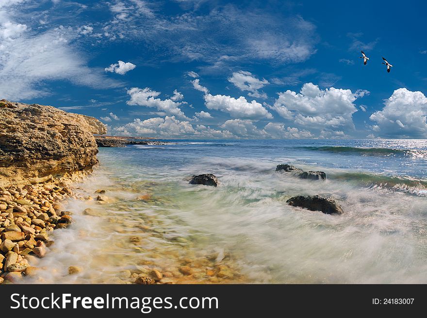 Seascape: sea and rocky coast, in the sky ducks fly, beautiful clouds on background