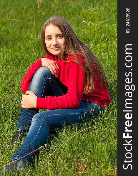 Beautiful teenage girl sitting in the grass on sunny spring day.