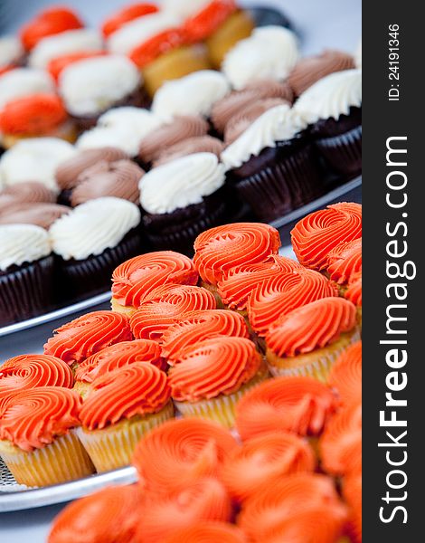 A whole bunch of cupcakes in orange and white. very shallow depth of field