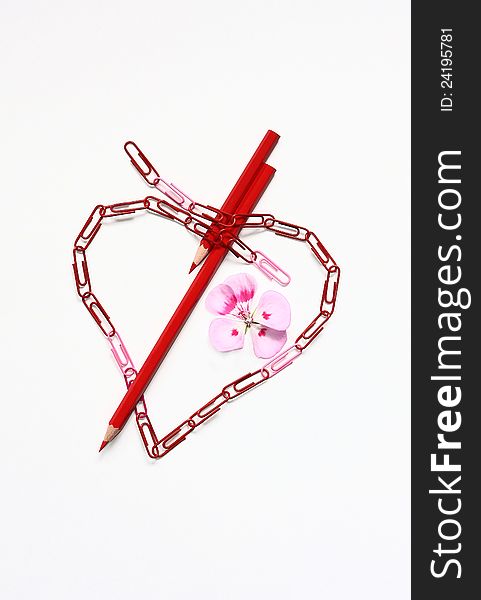 Abstract heart from paper clips is pierced by pencils.Nearby a flower.Background white. Abstract heart from paper clips is pierced by pencils.Nearby a flower.Background white.