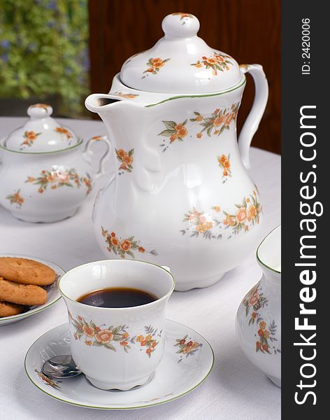 Coffee set on the table - cup of coffee on the front (focus on it) coffee pot, cookies and sugar bowl around.