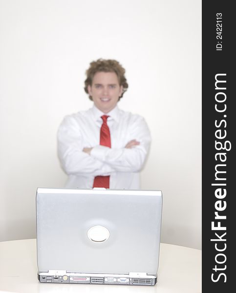 Businessman standing behind his laptop with his arms folded wearing a red tie. Businessman standing behind his laptop with his arms folded wearing a red tie