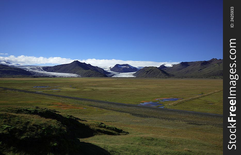 Icelandic Glacier over green fields against a blue sky