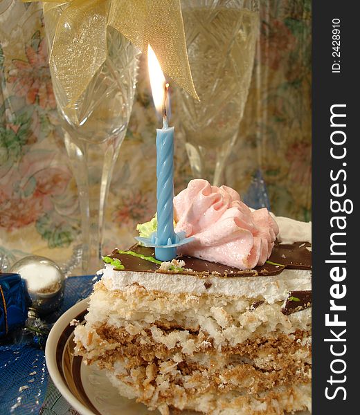Celebratory table (piece of birthday cake and blue candle, two glasses with champagne)