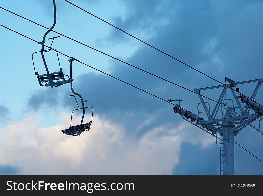 Chairlift with cables against blue sky with clouds in the early morning. Chairlift with cables against blue sky with clouds in the early morning