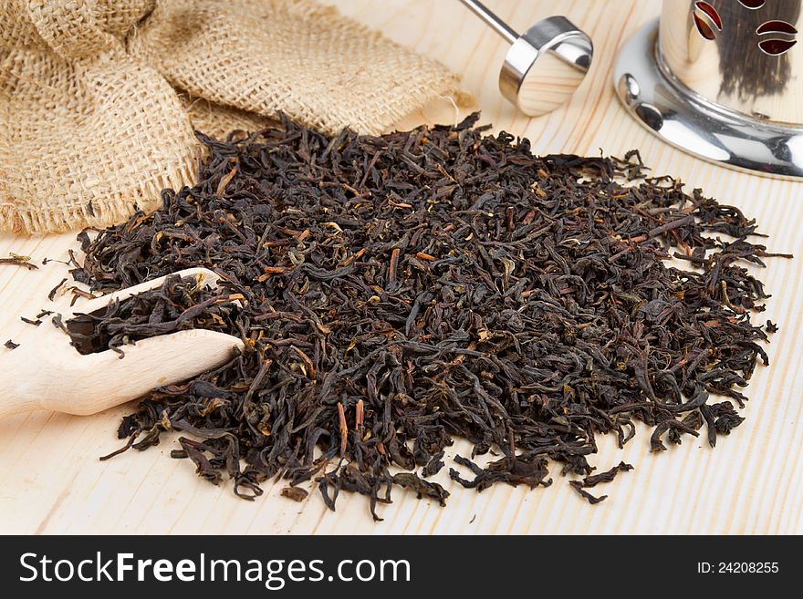 Black tea pile, wooden scoop, teapot on table