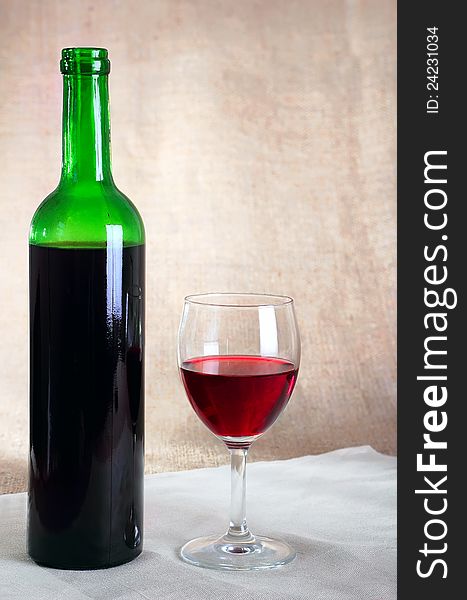 Bottle with red wine and a glass against a sacking