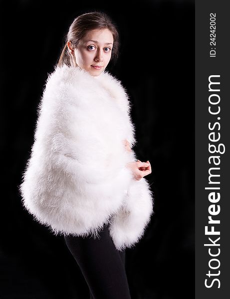 The beautiful dark-haired girl in a white fur coat on a black background, isolation. The beautiful dark-haired girl in a white fur coat on a black background, isolation