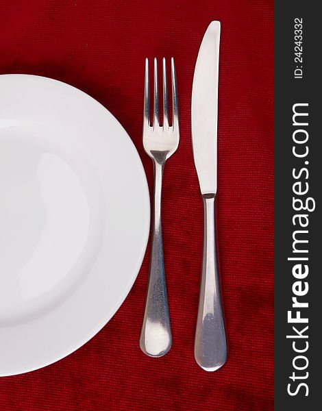 White plate, fork and knife on red background.