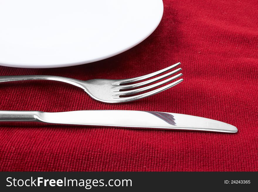 White plate fork and knife on red background.