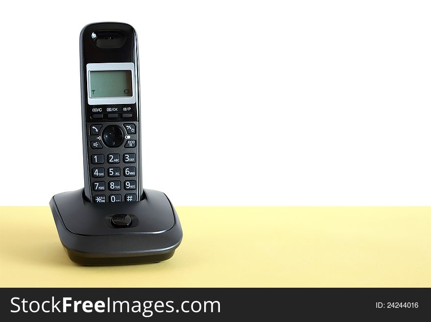 Modern black wireless telephone on yellow surface against white background. Clipping path is included