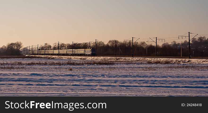 Electric locomotive with passenger cars running through winter prairie