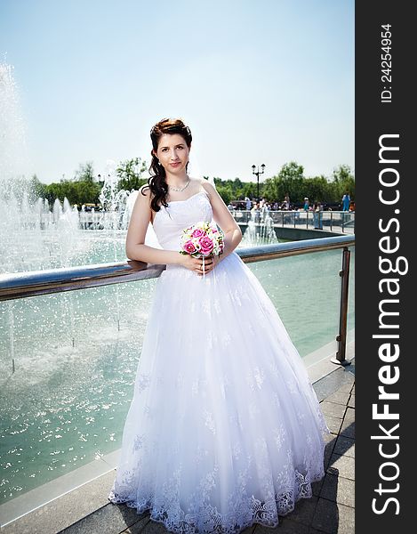 Happy bride about fountain with bouquet at wedding walk in the park