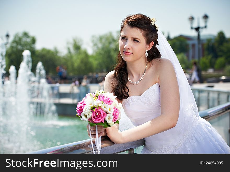 Happy bride about fountain with bouquet