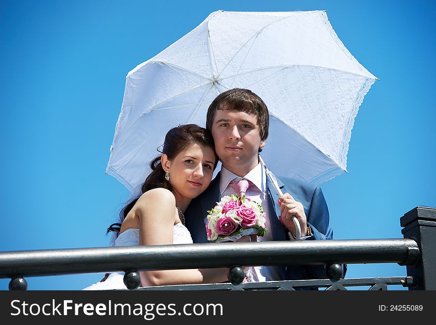 Happy bride and groom with umbrella at wedding walk