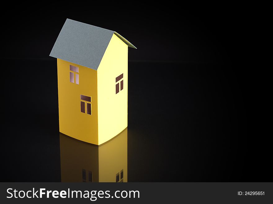 Nice yellow paper house with green roof on dark background with free space for text