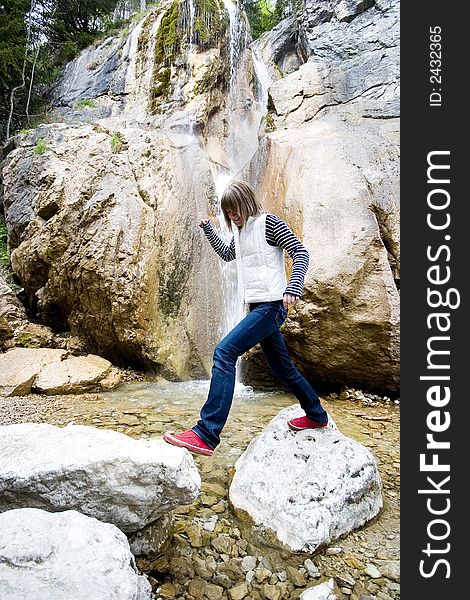 Little waterfall between big rocks and a jumping teen girl