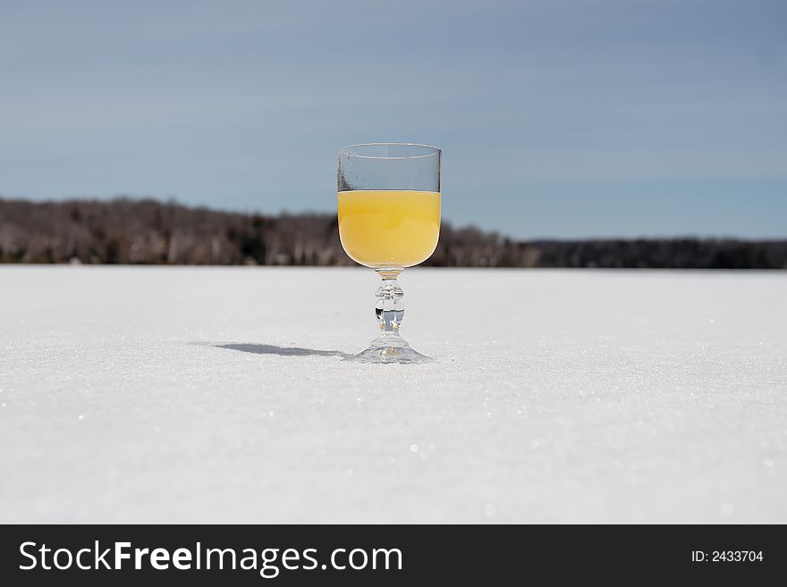 A glass of orange colored drink stands on a frozen lake. A glass of orange colored drink stands on a frozen lake