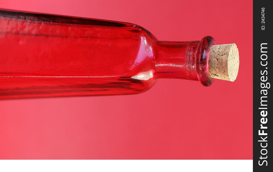 An emtpy red glass bottle with a cork in the top. Shoot against a red background