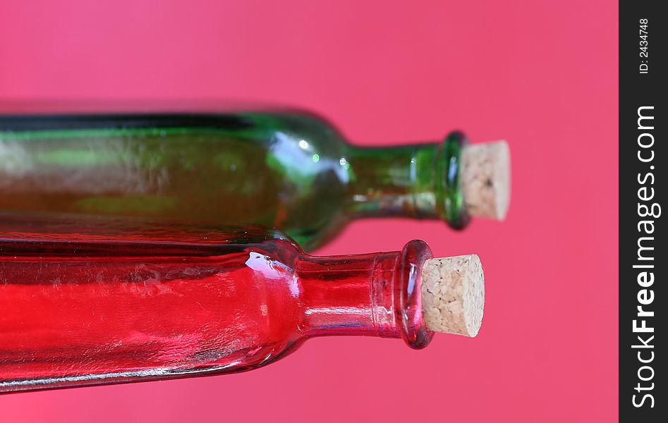 Emtpy red and green glass bottles with corks in the tops. Shot against a red background