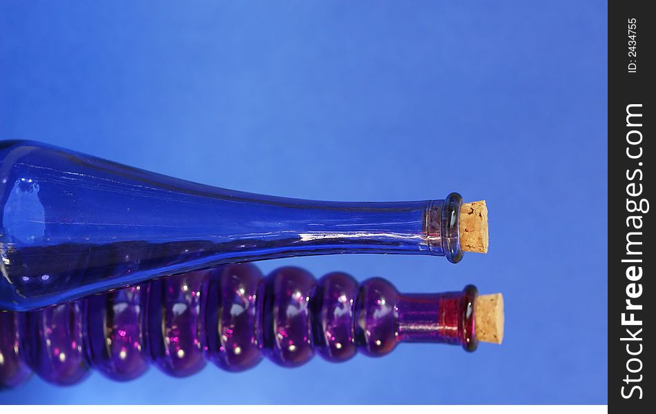 Empty blue and purple glass bottle with corks in the tops. Shot against a blue background. Empty blue and purple glass bottle with corks in the tops. Shot against a blue background