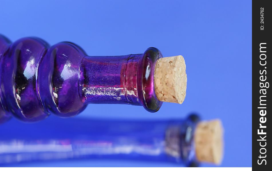 Empty blue and purple glass bottle with corks in the tops. Shot against a blue background. Empty blue and purple glass bottle with corks in the tops. Shot against a blue background