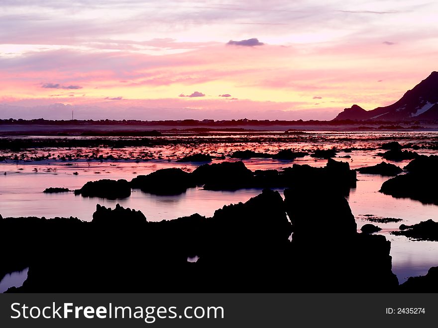 Landscape of an ocean at sunset with pink and purple sky and smooth water in Bettys Bay, South Africa. Landscape of an ocean at sunset with pink and purple sky and smooth water in Bettys Bay, South Africa.