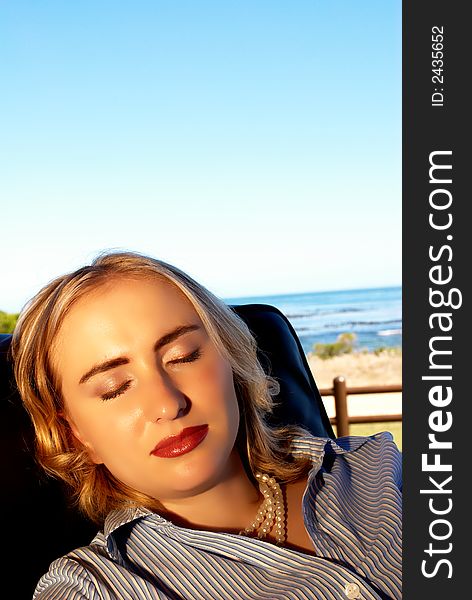 Young blonde woman sitting in leather chair enjoying her holiday by the ocean. Young blonde woman sitting in leather chair enjoying her holiday by the ocean.