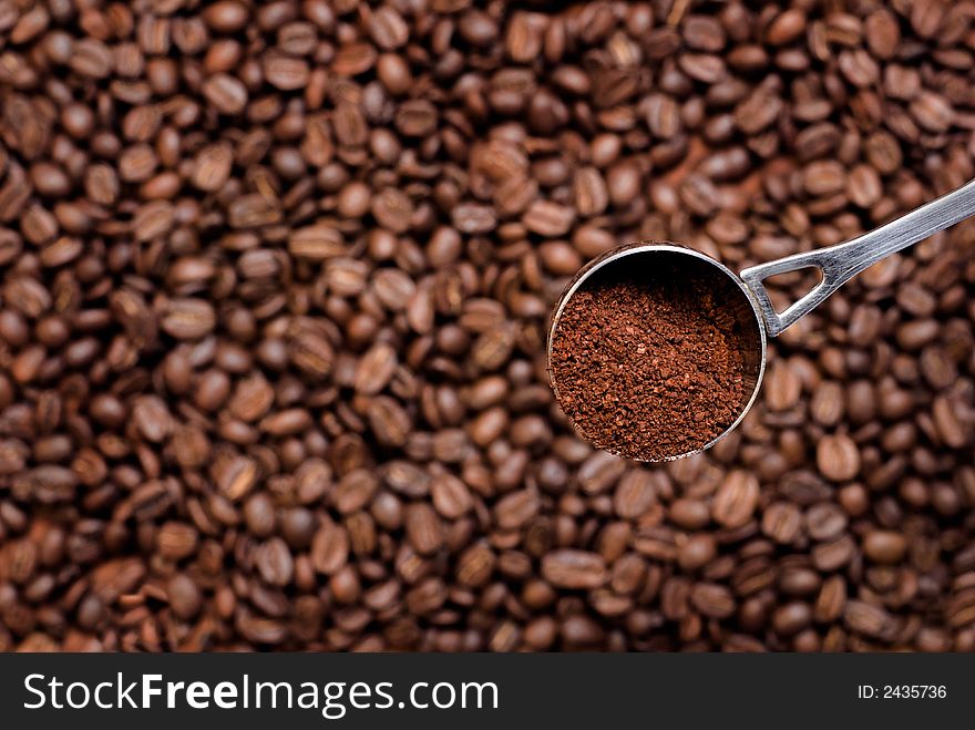 Spoon with grinded coffee (focus on it) over coffee seeds. Spoon with grinded coffee (focus on it) over coffee seeds.