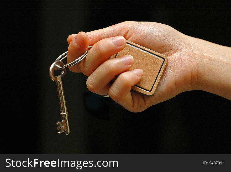 Outstretched hand holding a house key on an isolated black background. Outstretched hand holding a house key on an isolated black background