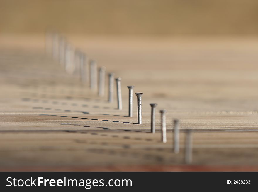 Line of nails in timber decking, only one nail in focus, very shallow depth of field.