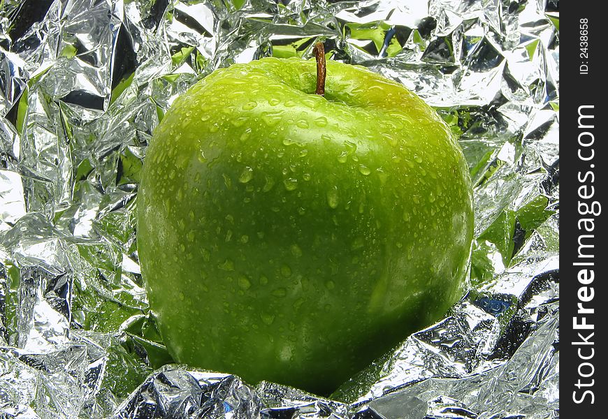 Green apple with drops on a metal, brilliant background.