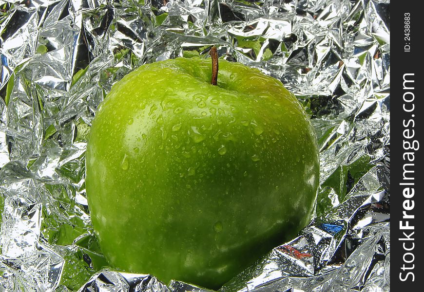 Green apple with drops on a metal, brilliant background.