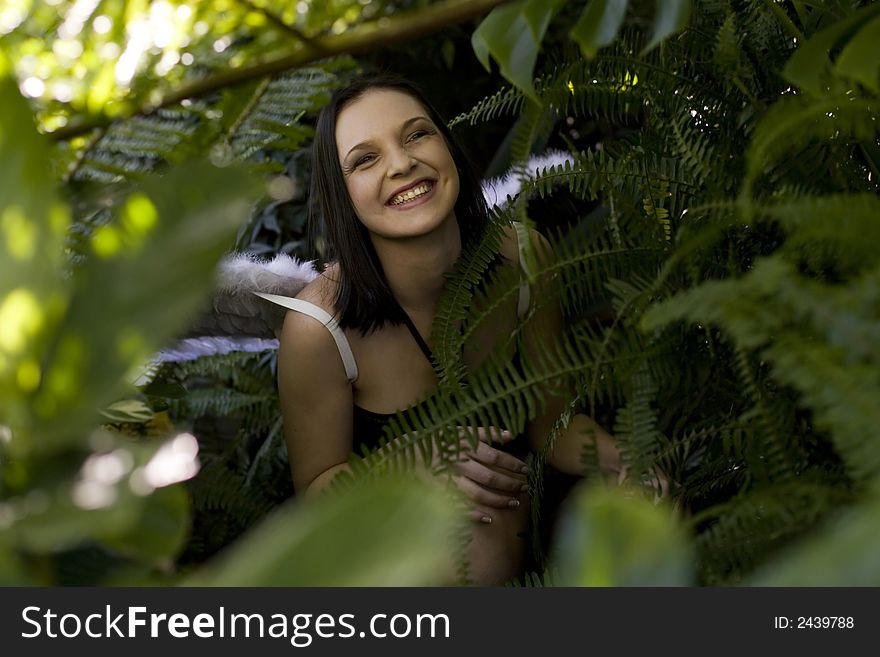 Laughing beautiful brunette fairy sitting in lots of green plants. Laughing beautiful brunette fairy sitting in lots of green plants