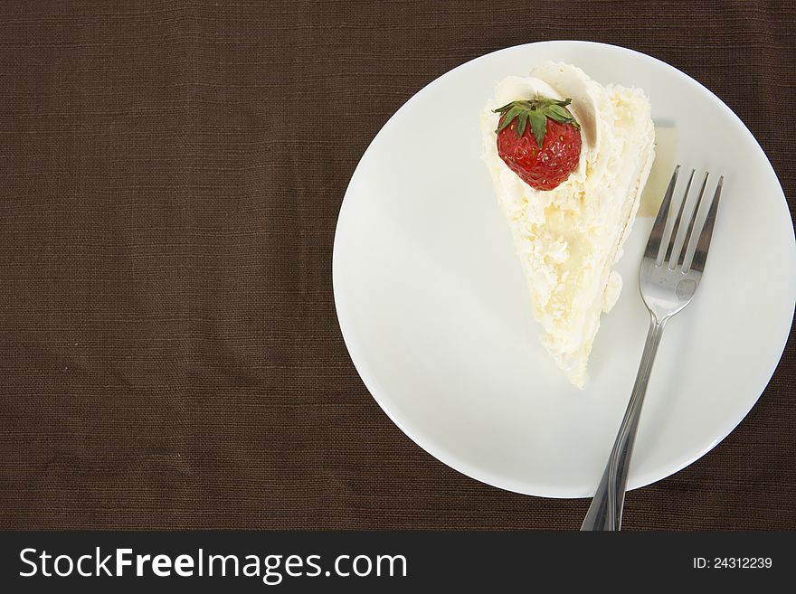 Delicious vanilla cake with strawberry decorate on top, on brown table mat, top view. Delicious vanilla cake with strawberry decorate on top, on brown table mat, top view