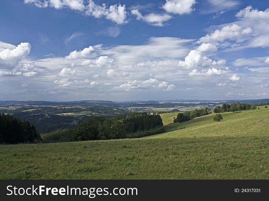 Hilly landscape with green meadows and forests with blue sky and clouds. Hilly landscape with green meadows and forests with blue sky and clouds