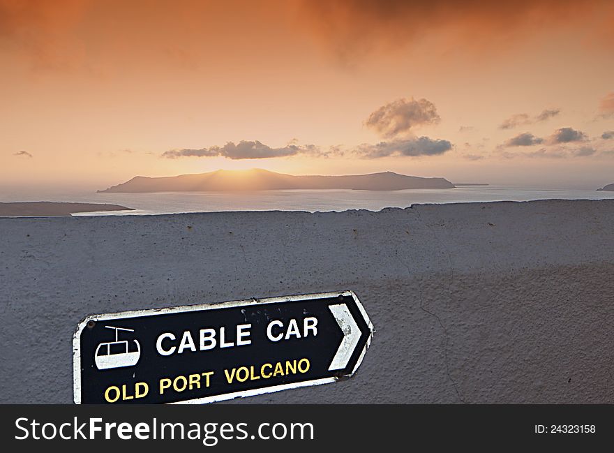 Sign for the cable car at Santorini island in Greece and the volcano during the sunset. Sign for the cable car at Santorini island in Greece and the volcano during the sunset