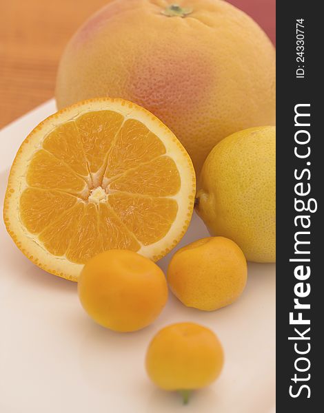 The group of citrus fruits on a white plate (lemon, orange, grapefruit, tangerine)