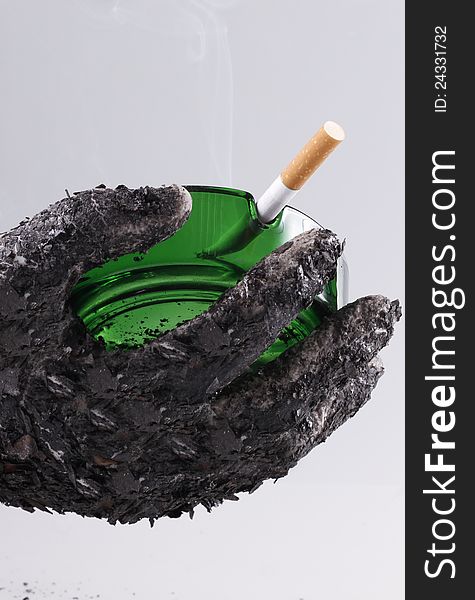 Ashed hand holding green ashtray with a fired cigarette which shows that smoking is harmful. Ashed hand holding green ashtray with a fired cigarette which shows that smoking is harmful