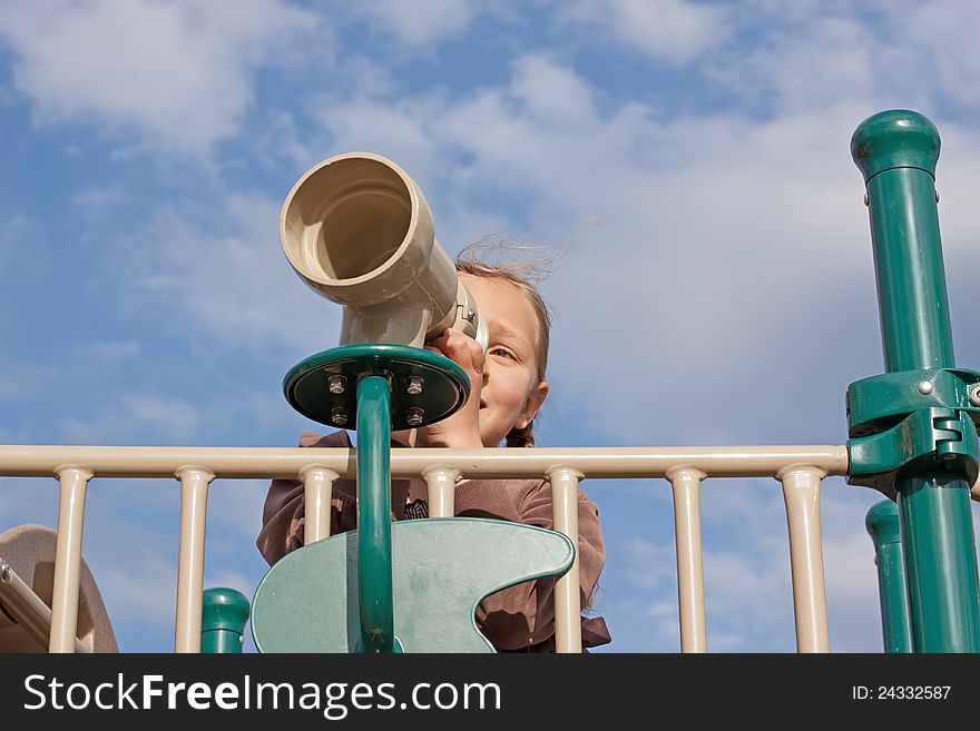A young girl looks through a telescope at the playground. A young girl looks through a telescope at the playground.