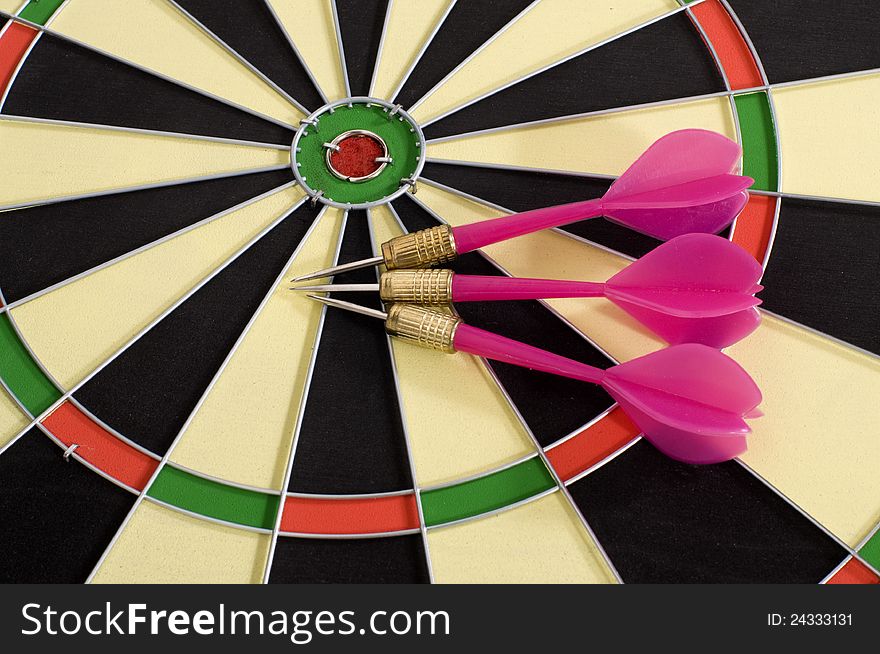 Three pink darts and circular dart board. Three pink darts and circular dart board