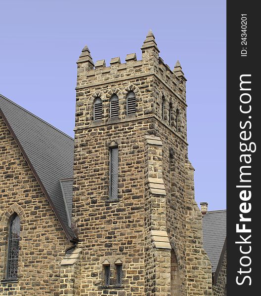 Square stone block fortress type bell tower on the corner of a church. Isolated against a blue sky. Square stone block fortress type bell tower on the corner of a church. Isolated against a blue sky.