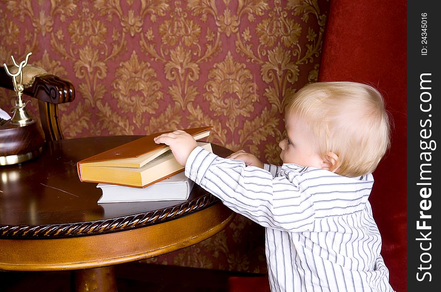Boy runs to the books lying on a table on a background of vintage wallpaper
