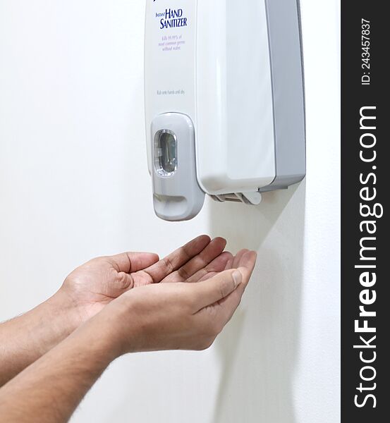 Hands placed under an automatic wall mounted sanitiser dispenser.