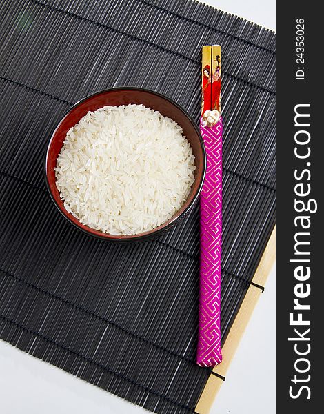 Bowl of rice with chopsticks from top on a black mat