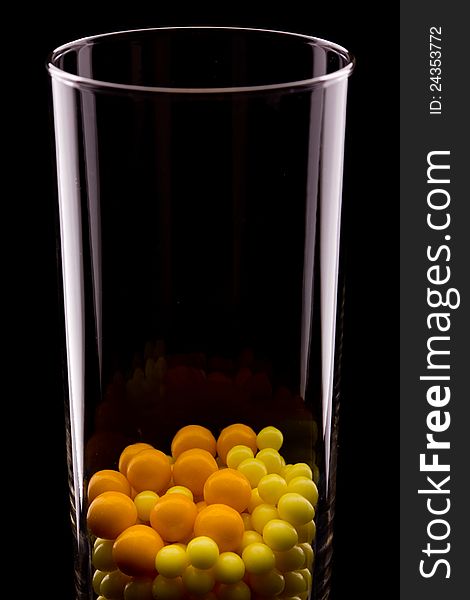 Glass with yellow round pills on black