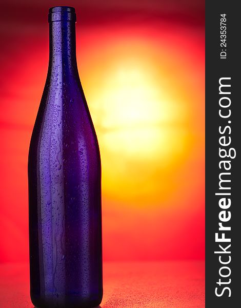 Opened blue glass bottle on sunset background